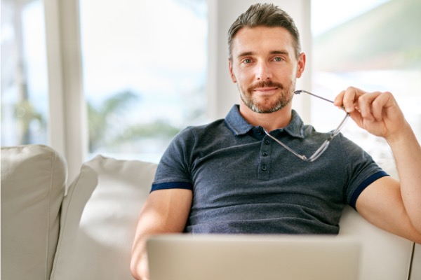 Man lookin at camera with laptop and glasses in hand